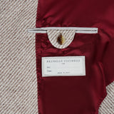 Close-up of the Water Resistant Cashmere Sport Jacket’s interior reveals a luxurious red satin lining, a buttoned pocket, and a white BRUNELLO CUCINELLI label with space for personal details, set against beige textured fabric. Exquisitely crafted in Italy by BRUNELLO CUCINELLI, this jacket exemplifies timeless sophistication.