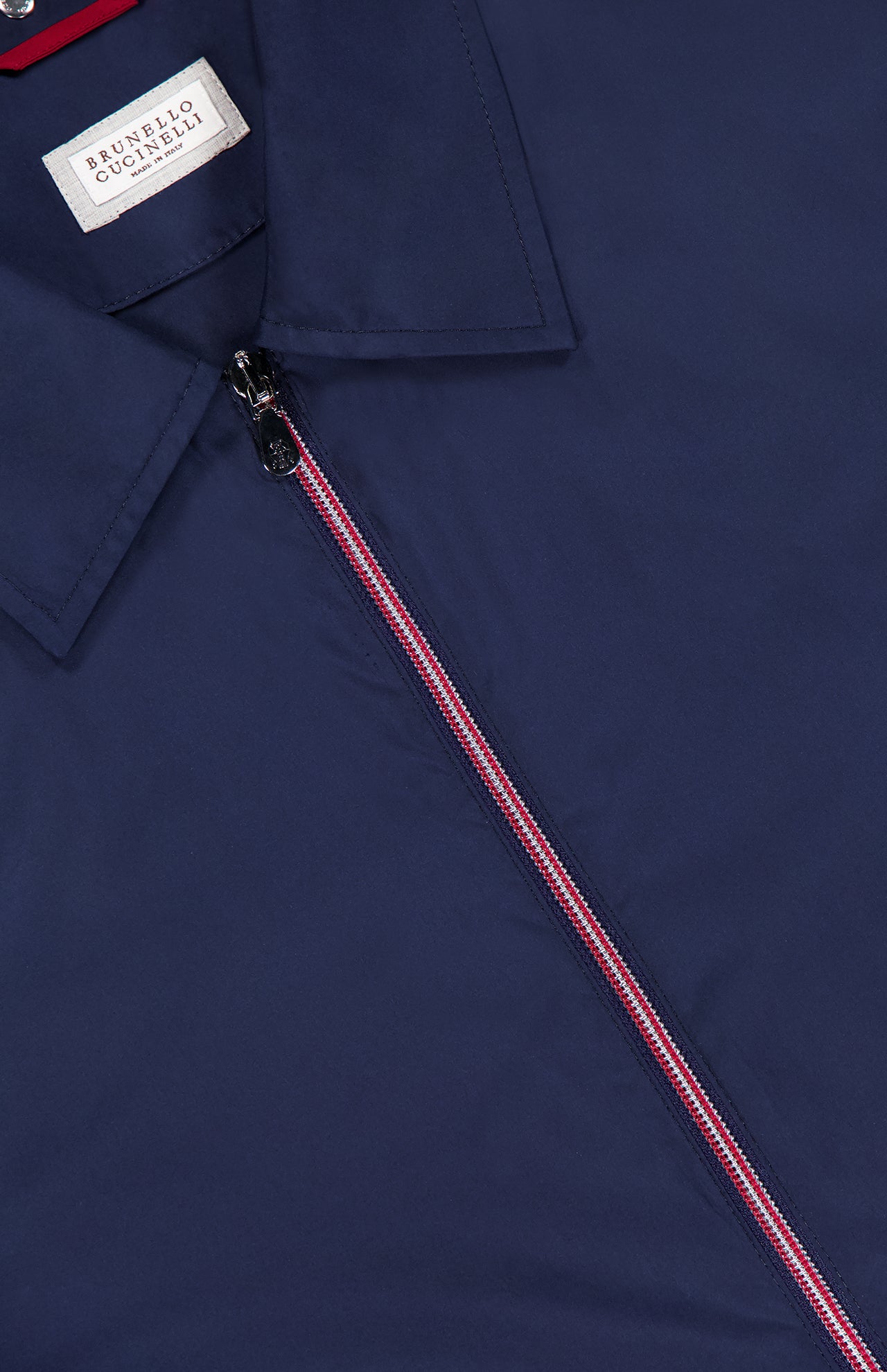 Close-up of a navy blue BRUNELLO CUCINELLI Water Resistant Contrast Zip Jacket for men, featuring a collar, zip with red and white accents, and visible brand label inside near the collar.
