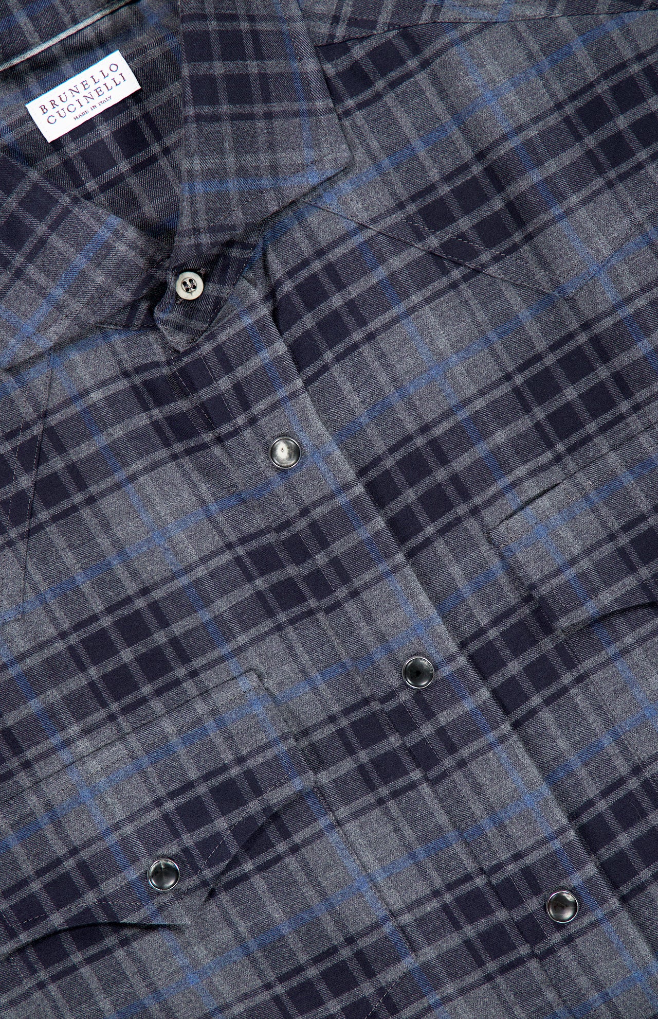 Close-up of the BRUNELLO CUCINELLI Western Cotton Plaid Shirt, featuring blue, gray, and black plaid with snap buttons and a visible brand label at the collar, crafted in the style of a cotton madras shirt.