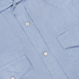 Close-up of the BRUNELLO CUCINELLI Cotton and Cashmere Western Shirt in light blue, featuring two chest pockets and pearl snap buttons for classic western wear appeal. The subtly textured fabric is highlighted, with a white BRUNELLO CUCINELLI label visible inside the collar.