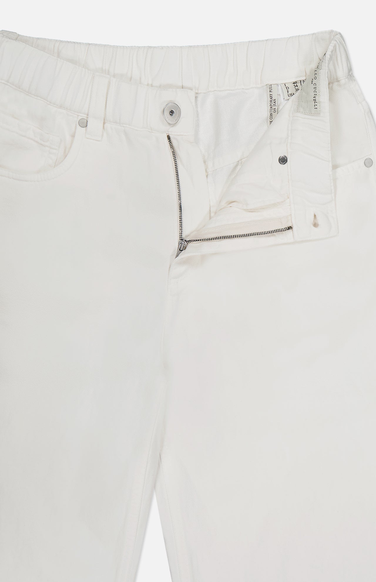 A close-up of BRUNELLO CUCINELLI Piece-Dyed Cotton Pull-On Jeans with an elastic waistband, partially unzipped fly, and visible interior tags, laid flat on a white background.