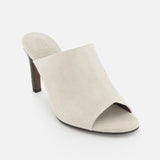 The BRUNELLO CUCINELLI Suede Curved Monili 80MM Mule Heel is a beige open-toe suede mule with a chunky brown heel and elegant monili embroidery, shown on a white background.