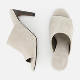 A pair of beige BRUNELLO CUCINELLI Suede Curved Monili 80MM Mule Heels is displayed from the side and top, showcasing open toes, block heels, and a minimalist design against a white background.