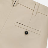 Close-up of BRUNELLO CUCINELLI Cotton Linen Bull Bermuda Pleated Short in beige; features a cotton-linen blend, waistband with belt loops, back pocket with button closure, and detailed stitching.