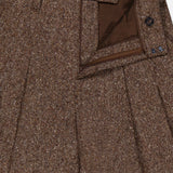 Close-up of BRUNELLO CUCINELLI Donegal Wool Barrel Pleated Pant in brown tweed, highlighting the pleated front, waistband with belt loops, open zipper, button closure, and a glimpse of the inside lining in a classic barrel fit.