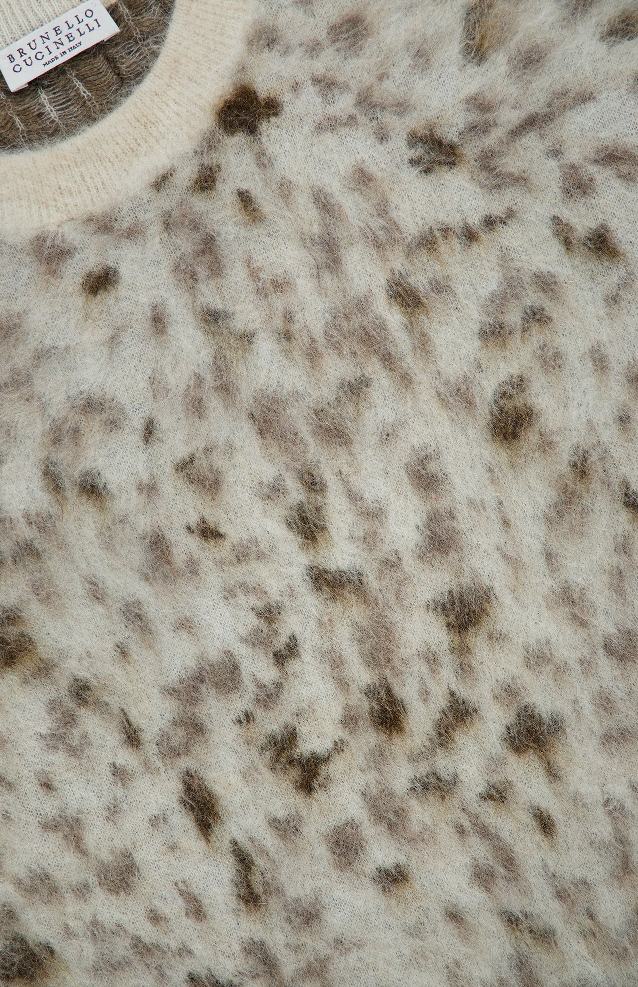 Close-up of a Brunello Cucinelli Jacquard Mohair Knitted Long Sleeve Sweater in fuzzy cream mohair wool with an abstract brown lynx jacquard pattern and a ribbed neckline.