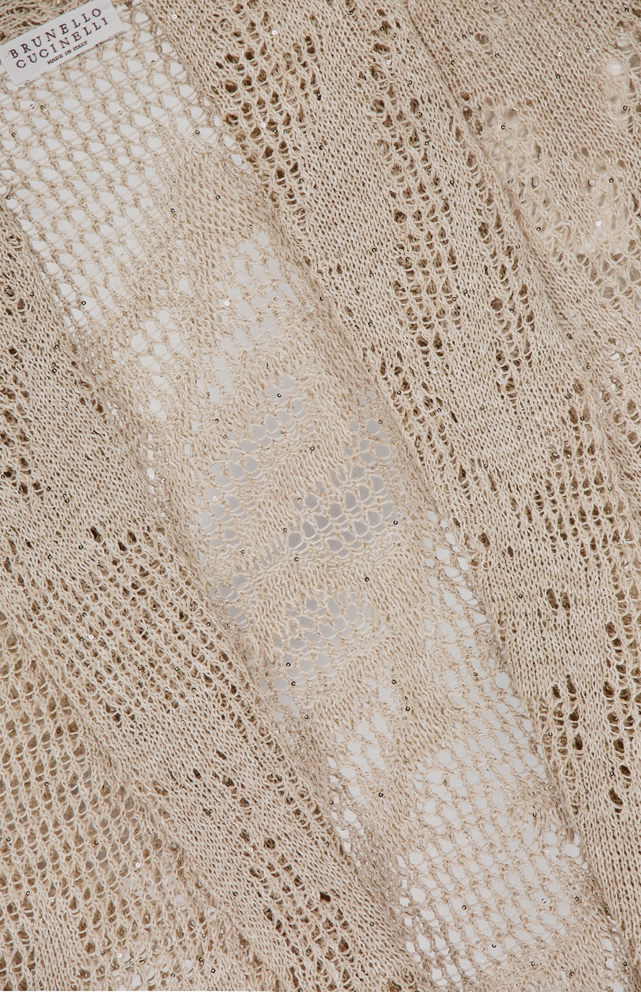Close-up of the Linen Cotton Shawl Collar Cardigan by BRUNELLO CUCINELLI, showcasing light beige knit, intricate texture, and delicate lace effect. The brand’s white label appears in the upper left corner.