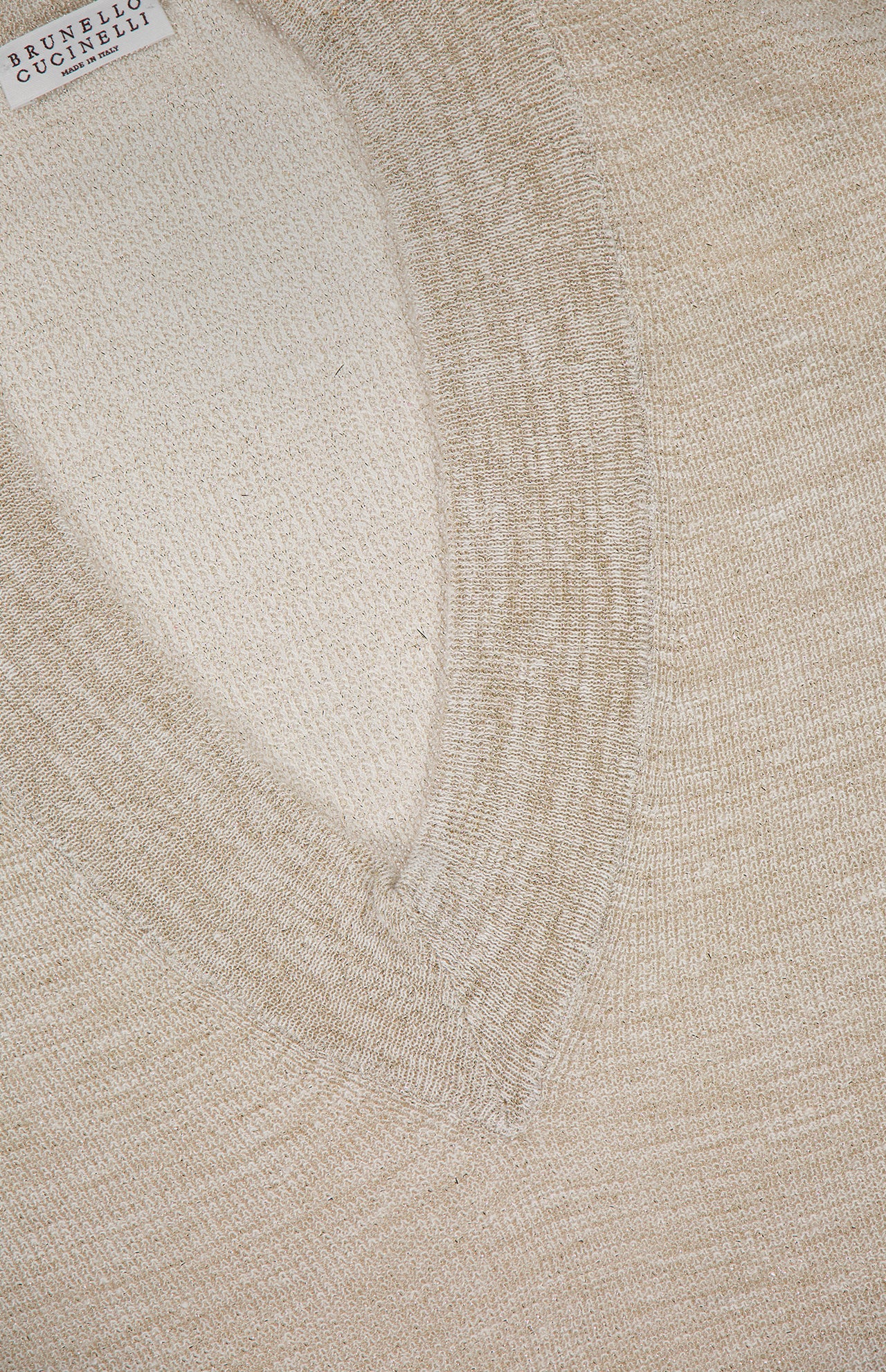Close-up of a beige BRUNELLO CUCINELLI Linen Long Sleeve V-Neck Pullover Sweater, featuring textured knit fabric and a visible brand label in the upper left corner.