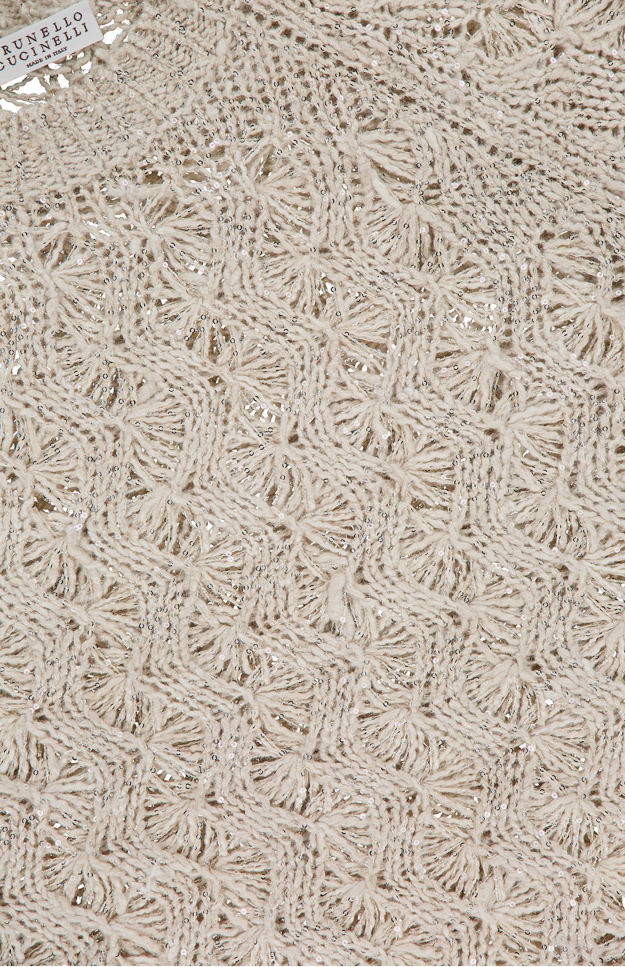 Close-up of a cream Linen Silk Cable Short Sleeve Knit Sweater by BRUNELLO CUCINELLI, featuring an intricate geometric pattern with metallic threads and a visible brand tag in the top left corner.