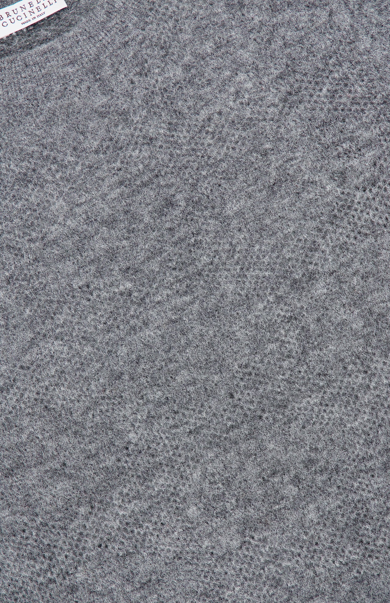 Close-up of a heather gray textured knit fabric with a subtle pattern, featuring part of the clothing label in the upper left corner, echoing the refined craftsmanship of the BRUNELLO CUCINELLI Silk Knitted Long Sleeve Sweater.