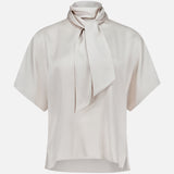 The BRUNELLO CUCINELLI Silk Satin Short Sleeve Blouse in light beige features a loose fit, short sleeves, and a high neck tie detail, shown against a plain white background.