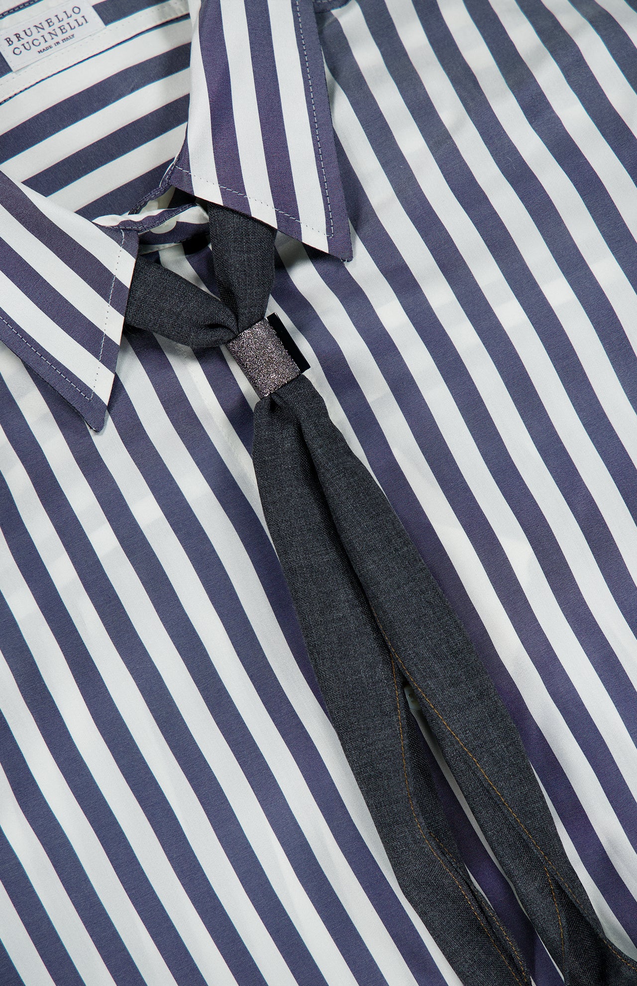 Brunello Cucinelli Silk Striped Refined Western Blouse in navy and white vertical stripes, worn with a dark grey necktie fastened by a small metallic clip and Mother of Pearl buttons.