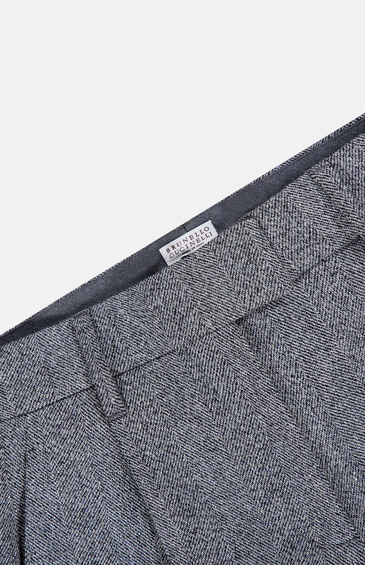 Close-up of the Sparkling Herringbone Loose Pleated Pant in silver-grey wool with prominent pleats and a visible BRUNELLO CUCINELLI label on the inner waistband, showcasing refined craftsmanship and classic Italian style.