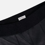 Close-up of the Stretch Leather Legging by BRUNELLO CUCINELLI, crafted in black leather with vertical stitching and a black elastic waistband. A white label bearing the brand’s name is visible, highlighting the refined womenswear aesthetic and modern silhouette of these sleek leggings.