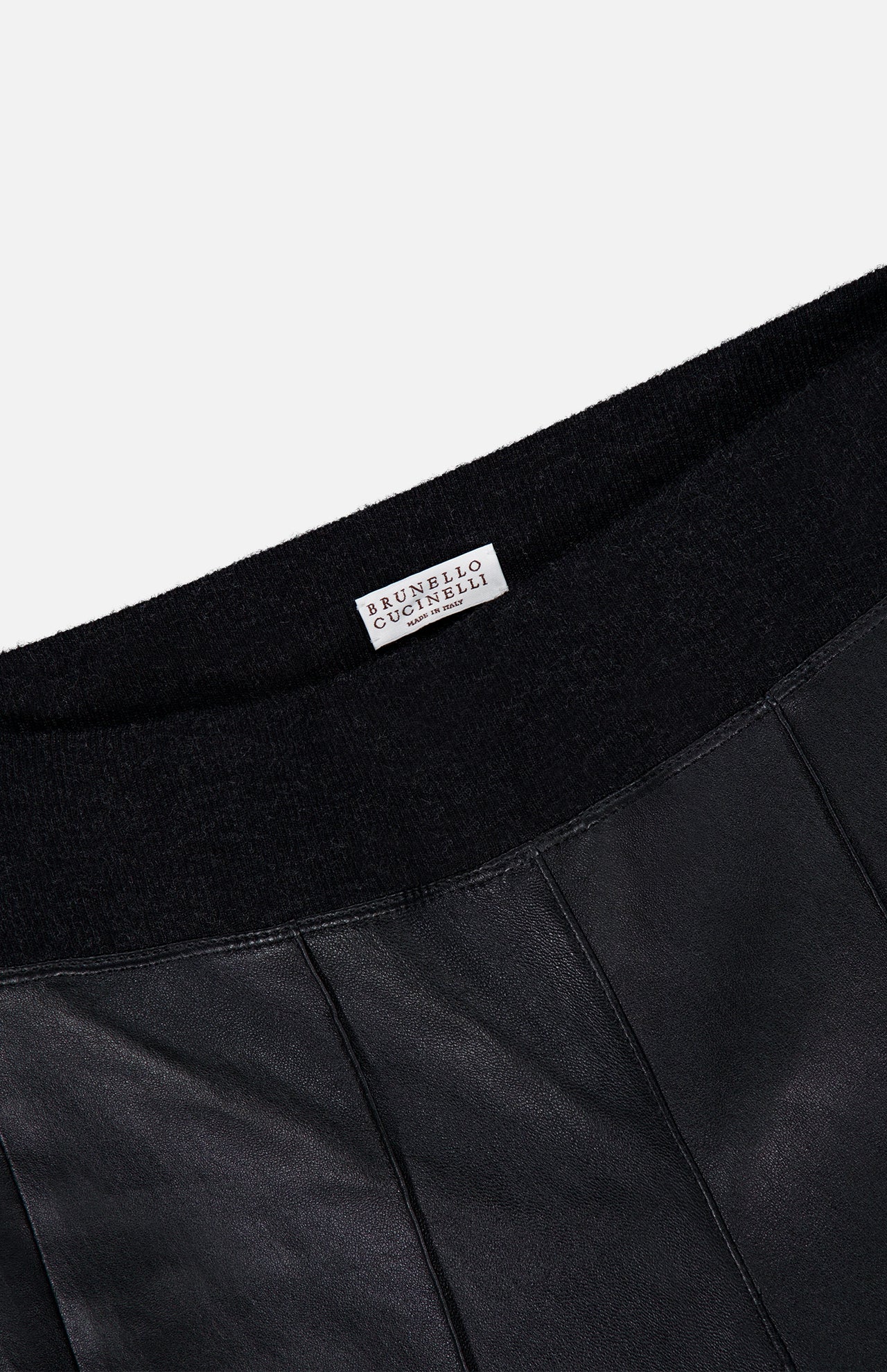 Close-up of the Stretch Leather Legging by BRUNELLO CUCINELLI, crafted in black leather with vertical stitching and a black elastic waistband. A white label bearing the brand’s name is visible, highlighting the refined womenswear aesthetic and modern silhouette of these sleek leggings.