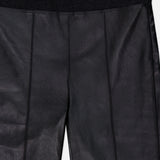 Close-up of the BRUNELLO CUCINELLI Stretch Leather Legging, crafted from black faux leather with visible seams and a black elastic waistband in a modern womenswear style. A white tag with text is sewn at the center of the waistband, highlighting these chic stretch leggings.