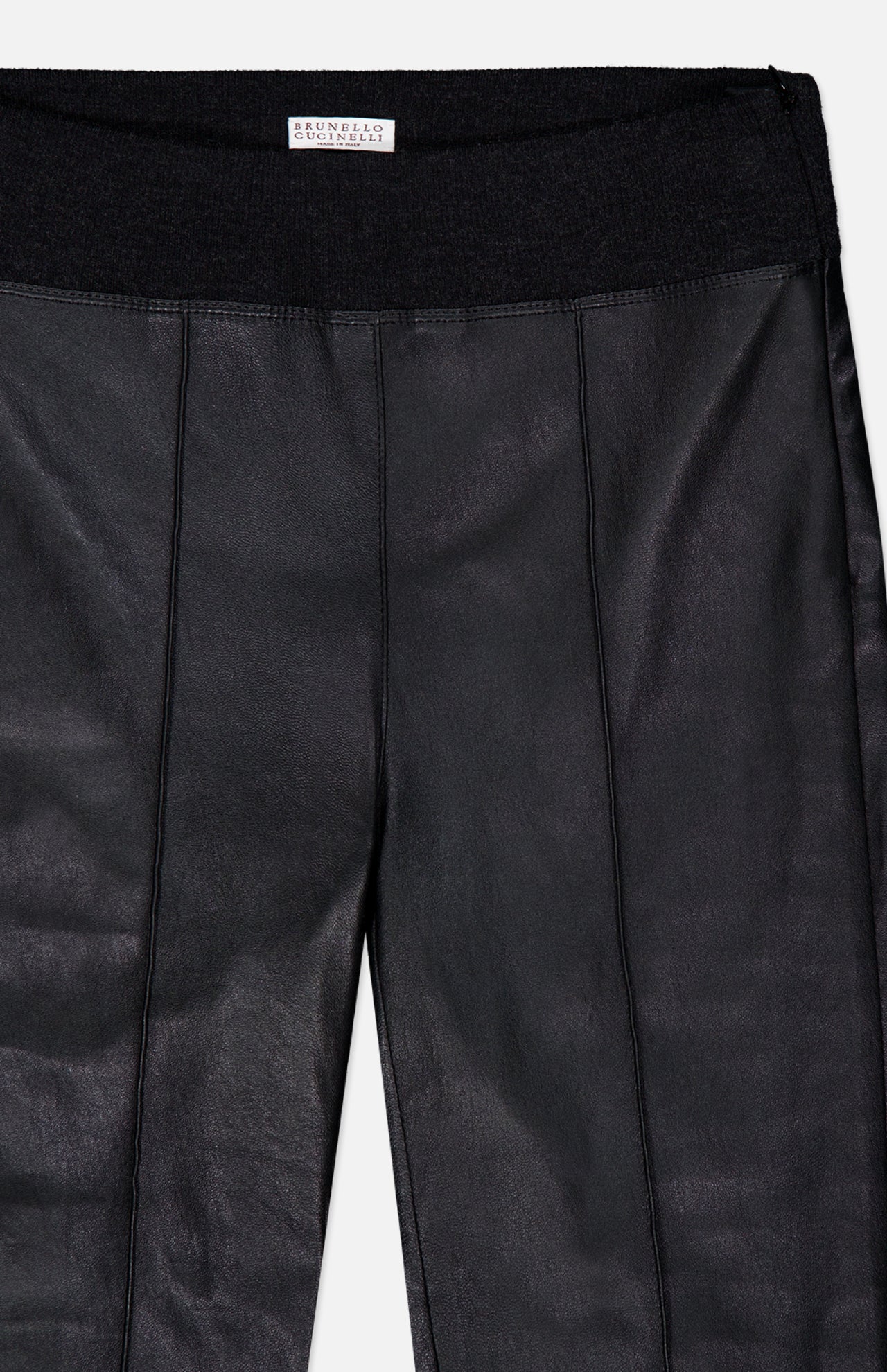 Close-up of the BRUNELLO CUCINELLI Stretch Leather Legging, crafted from black faux leather with visible seams and a black elastic waistband in a modern womenswear style. A white tag with text is sewn at the center of the waistband, highlighting these chic stretch leggings.