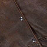Close-up of the BRUNELLO CUCINELLI Vintage Aviator Shearling Vest in brown leather, featuring visible texture, metal snap buttons, and a touch of fur trim along the left side. Geometric stitching patterns accentuate the aviator-inspired design and highlight the subtle shearling lining.