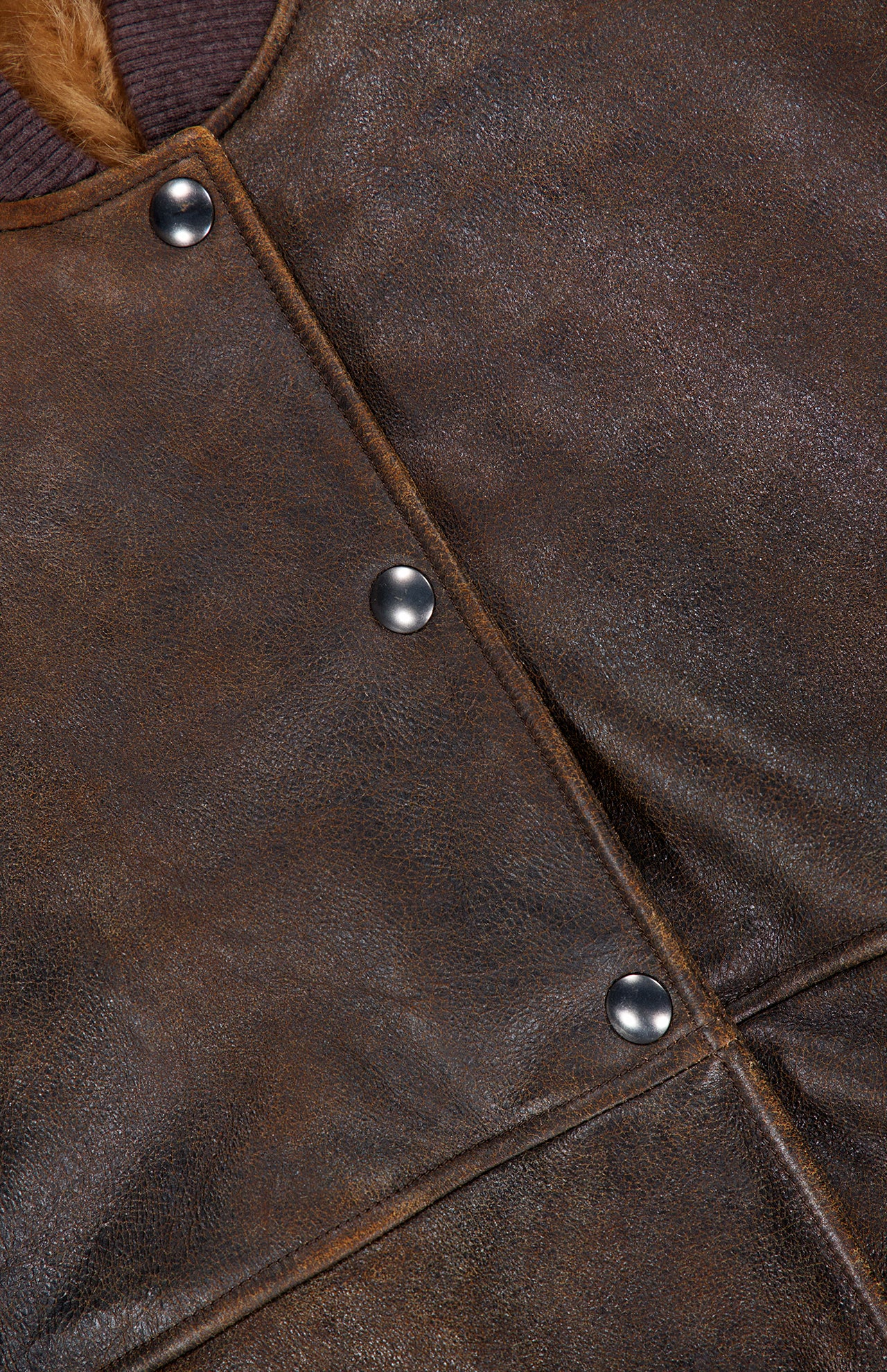 Close-up of the BRUNELLO CUCINELLI Vintage Aviator Shearling Vest in brown leather, featuring visible texture, metal snap buttons, and a touch of fur trim along the left side. Geometric stitching patterns accentuate the aviator-inspired design and highlight the subtle shearling lining.