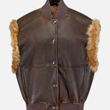 The Vintage Aviator Shearling Vest from BRUNELLO CUCINELLI features a brown leather exterior with tan fur trim along the armholes, a dark ribbed collar and hem, and snap button front closure. This aviator-style vest is finished with classic details and a cozy shearling lining for enhanced warmth and comfort.
