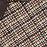 Here’s a revised version using the provided product data: Close-up of the Vintage Wool Check Print Bomber Jacket by BRUNELLO CUCINELLI, showcasing a brown checked wool fabric in a houndstooth pattern with tones of brown, black, and white, complemented by a dark brown leather collar partially visible in the upper left corner—an elegant piece that echoes Brunello Cucinelli’s signature timeless style.
