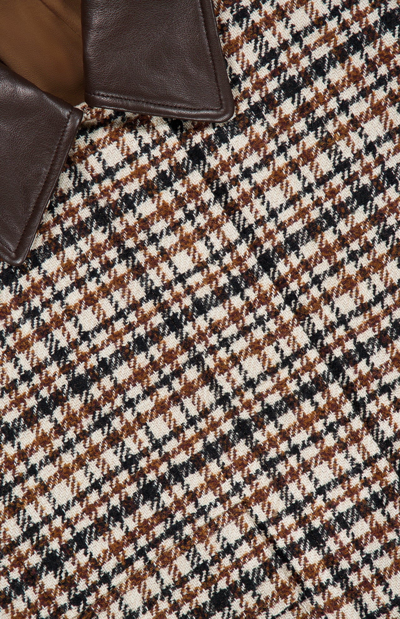 Here’s a revised version using the provided product data: Close-up of the Vintage Wool Check Print Bomber Jacket by BRUNELLO CUCINELLI, showcasing a brown checked wool fabric in a houndstooth pattern with tones of brown, black, and white, complemented by a dark brown leather collar partially visible in the upper left corner—an elegant piece that echoes Brunello Cucinelli’s signature timeless style.