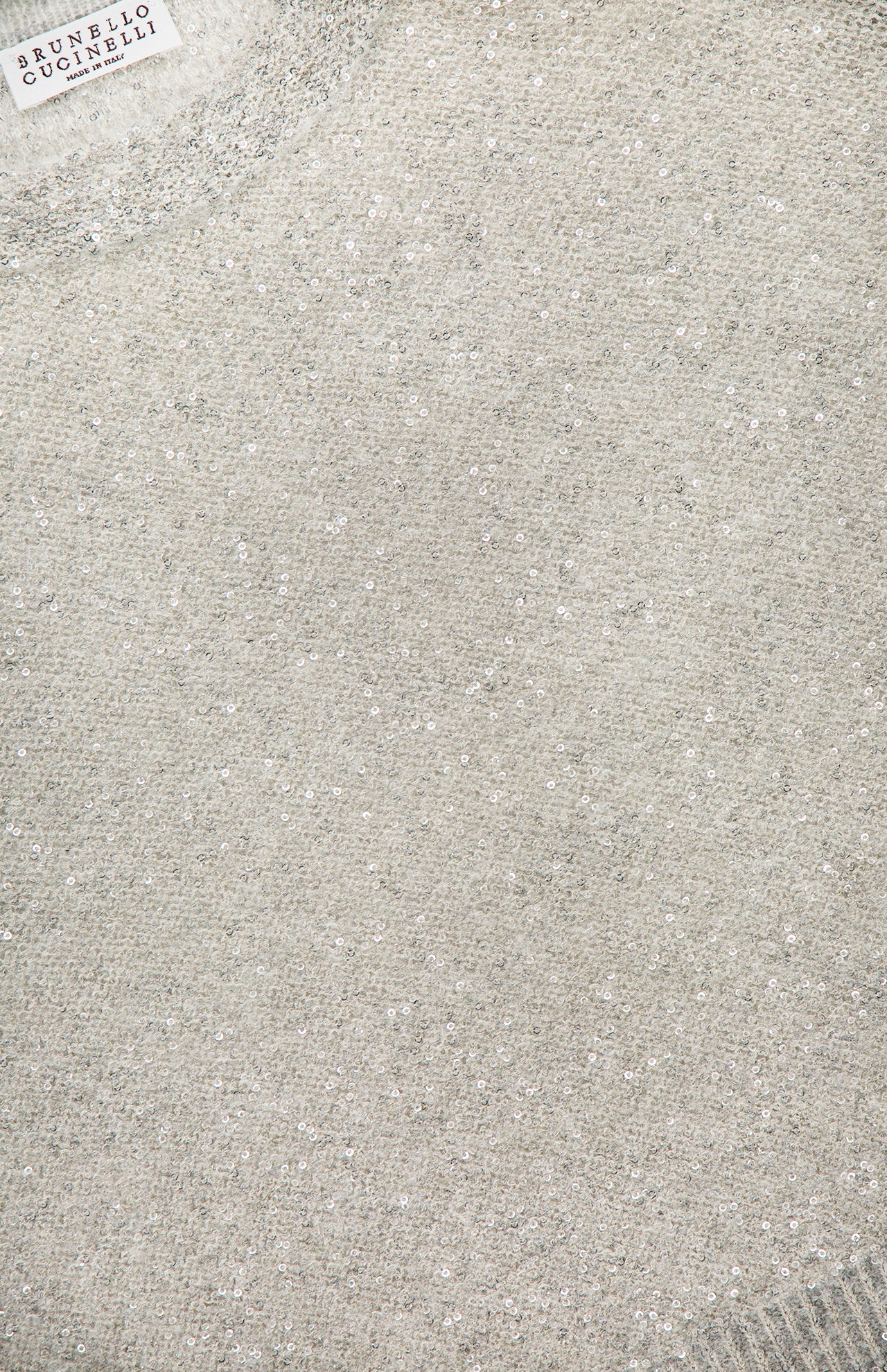 Close-up of a light gray BRUNELLO CUCINELLI Wool Mohair Pailette Crewneck Sweater, featuring a sparkly, glitter-like texture reminiscent of sequins and the brand label visible in the top left corner.