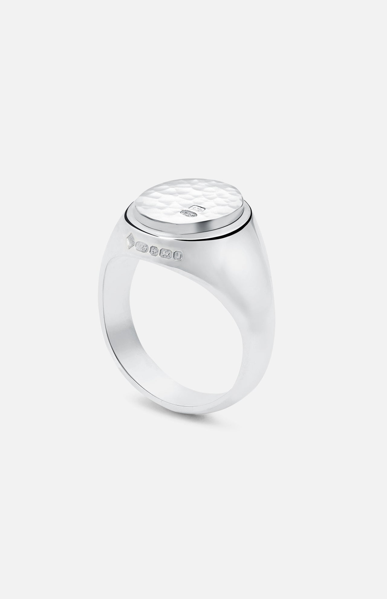 The BUNNEY Oval Signet Ring features a hammered-texture, oval sterling silver face with hallmark side stamps, showcased on a white background—a refined piece of handmade UK jewelry craftsmanship.