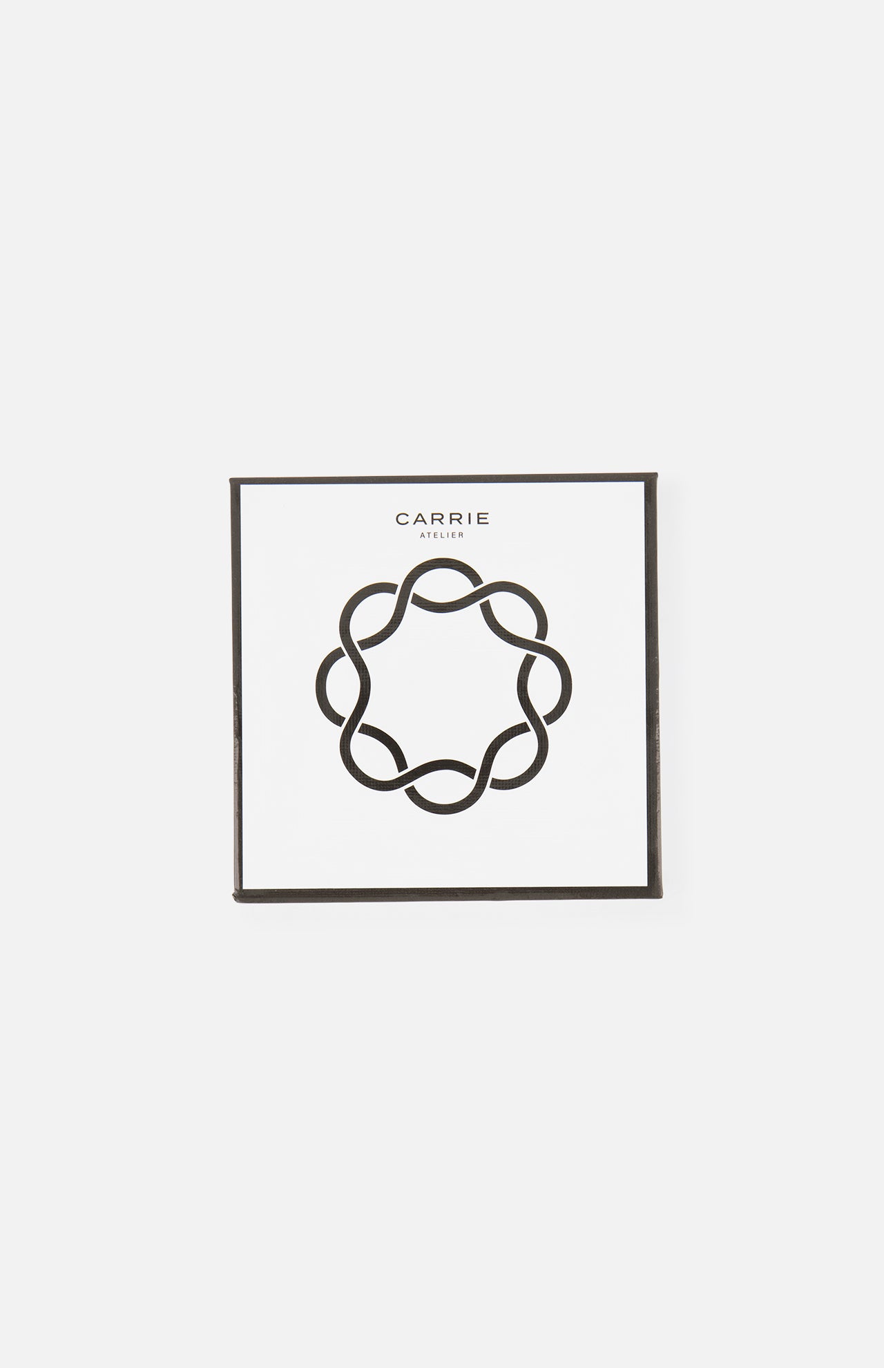 A square white card with a thin black border features a black abstract circular design and CARRIE ATELIER above it, ideal for displaying the Carrie Purse Hook in Silver.