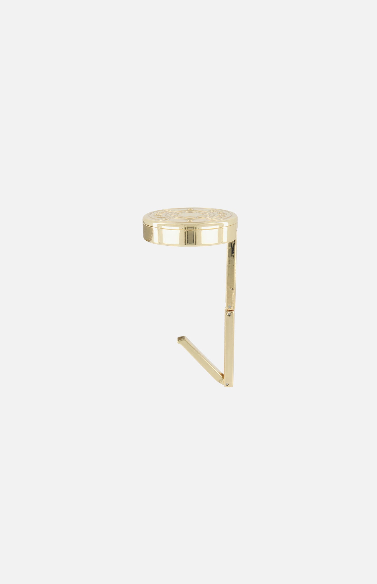 The CARRIE ATELIER Carrie Purse Hook in Yellow Gold is a small, circular, engraved table with a slim L-shaped leg, designed as a portable purse hanger and anti-slip bag holder shown on a plain white background.