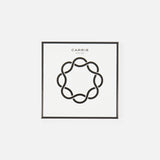 A white square box with a black abstract circle in the center and “CARRIE” above—stylish packaging for the Carrie Purse Hook Suede Etoile in Rose Eclipse by CARRIE ATELIER, a chic designer bag accessory.