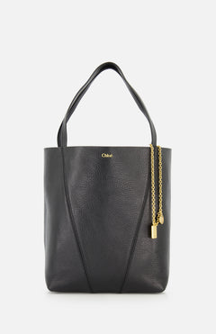 The Chloé Spin Bag with Chain by CHLOÉ is a black leather tote with two handles, gold branding near the top, and a removable chain featuring a padlock and key charm on the side.