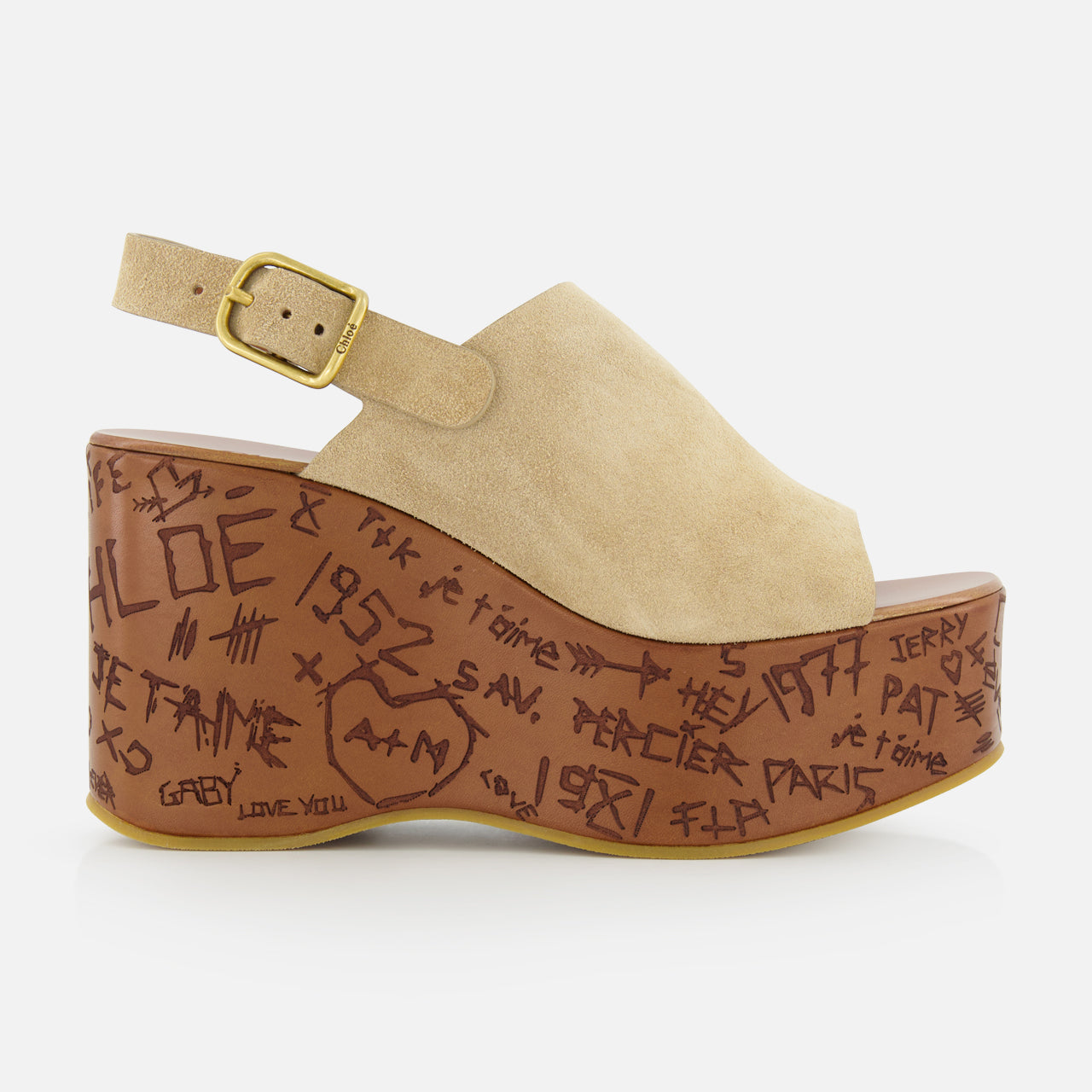 The Maxime Carved Wedge Heel by CHLOÉ is a beige suede platform sandal, made in Italy, featuring a gold buckle, thick brown sole, and dark brown graffiti-style doodles alongside hand-drawn symbols.