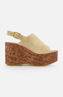 The Maxime Carved Wedge Heel by CHLOÉ is a beige suede platform sandal, made in Italy, featuring a gold buckle, thick brown sole, and dark brown graffiti-style doodles alongside hand-drawn symbols.