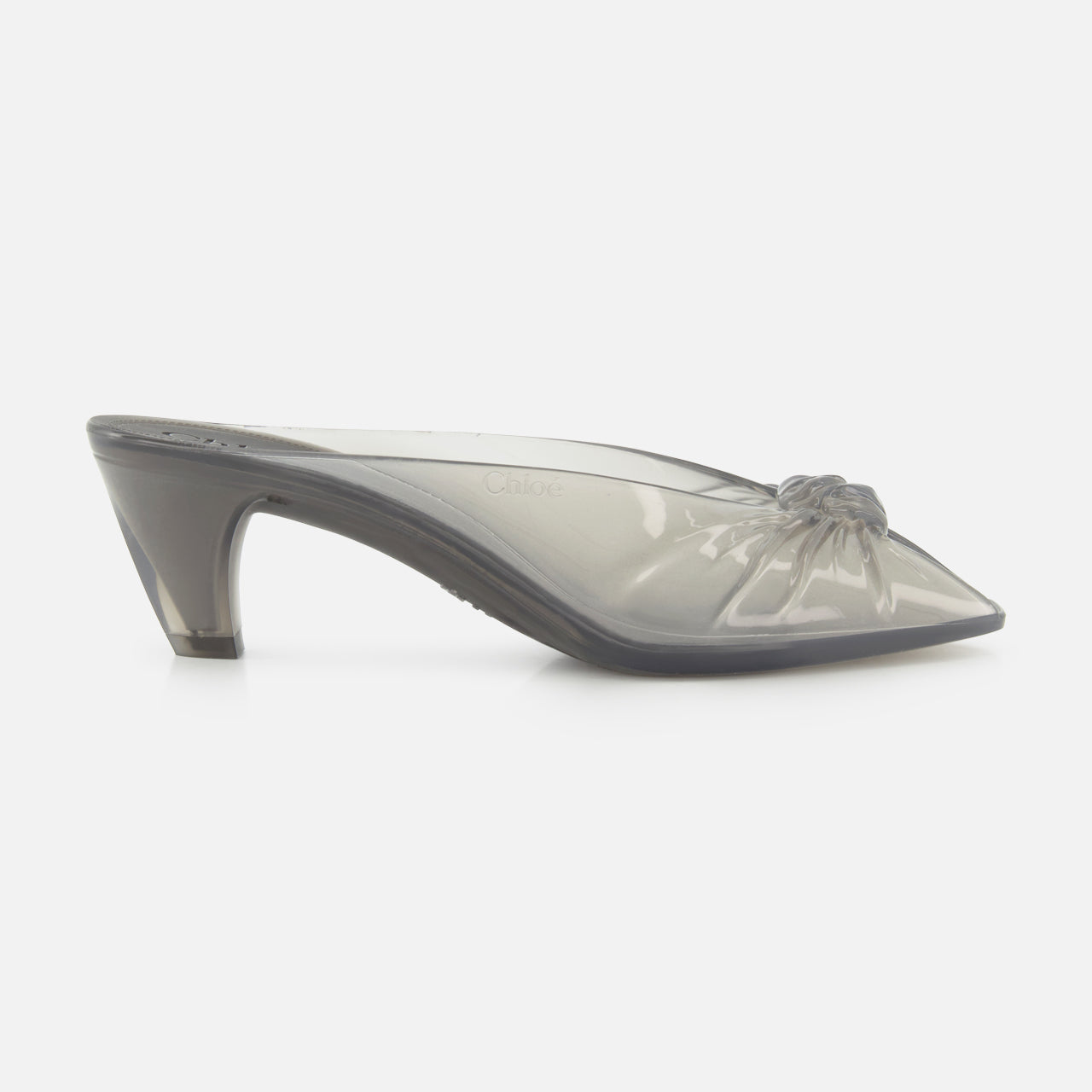 The CHLOÉ Chlóe Jelly Mule is a translucent gray heeled mule with a pointed toe and decorative bow on the upper, showcased against a plain white background.