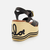 The CHLOÉ Chlóe Sand Wedge Heel features black leather straps, a gold buckle, a thick natural woven platform sole, and black embroidery spelling the Chloé logo on the heel.