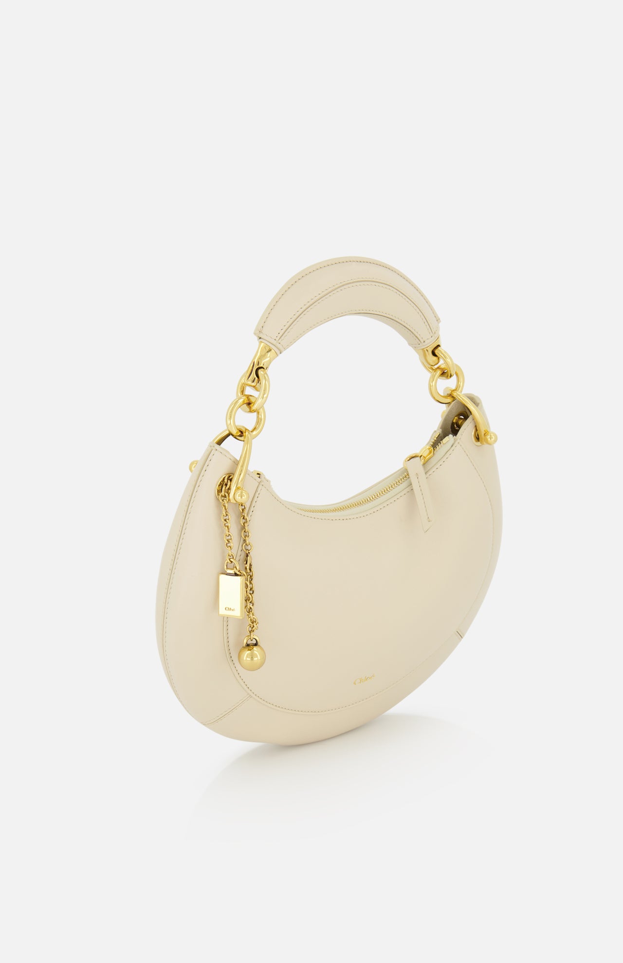 The Chloé Slim Banana Bag by CHLOÉ, crafted in Italy in a milk tone, features a curved shape, gold hardware, a leather top handle, and elegant gold chain accents, shown on a plain white background.