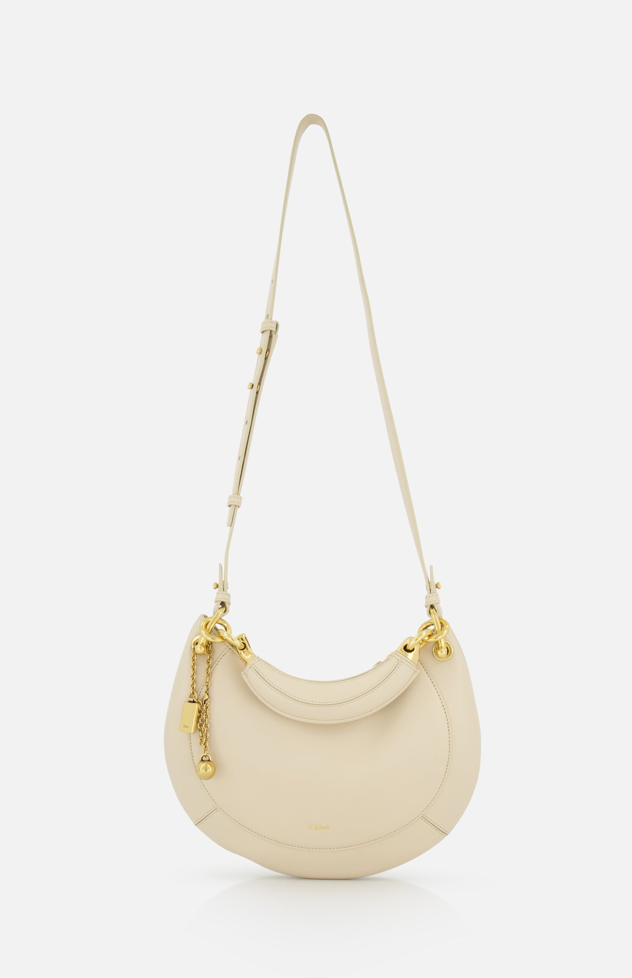 The CHLOÉ Slim Banana Bag is a cream-toned, crescent-shaped handbag with gold hardware, a long adjustable strap, and leather top handle. Made in Italy, it features a small gold keychain and lock detail on one side.