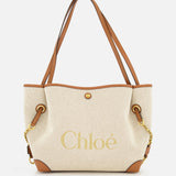 Introducing the Chloé Cotton Clover Bag by CHLOÉ—a beige canvas cotton tote featuring brown leather handles and trim, gold chain accents, and “Chloé” elegantly printed in gold on the front. This versatile designer bag effortlessly blends style and function, making it a perfect choice for the office.