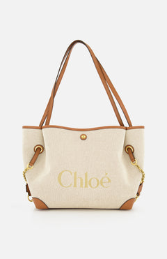 Introducing the Chloé Cotton Clover Bag by CHLOÉ—a beige canvas cotton tote featuring brown leather handles and trim, gold chain accents, and “Chloé” elegantly printed in gold on the front. This versatile designer bag effortlessly blends style and function, making it a perfect choice for the office.