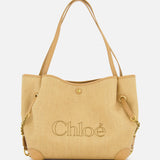 Introducing the Chloé Raffia Clover Bag: a beige woven raffia tote featuring leather handles, gold chain accents, and sleek leather trim. The brand name CHLOÉ is boldly embroidered on the front, complemented by grommet details near the handles and a secure snap closure.