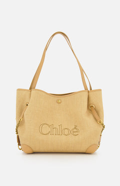 Introducing the Chloé Raffia Clover Bag: a beige woven raffia tote featuring leather handles, gold chain accents, and sleek leather trim. The brand name CHLOÉ is boldly embroidered on the front, complemented by grommet details near the handles and a secure snap closure.