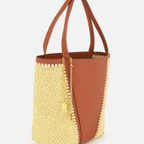The CHLOÉ Woven Panels Spin Bag is a two-tone brown leather tote with yellow raffia-inspired woven side panels, double handles, and a gold chain padlock charm, shown against a white background.
