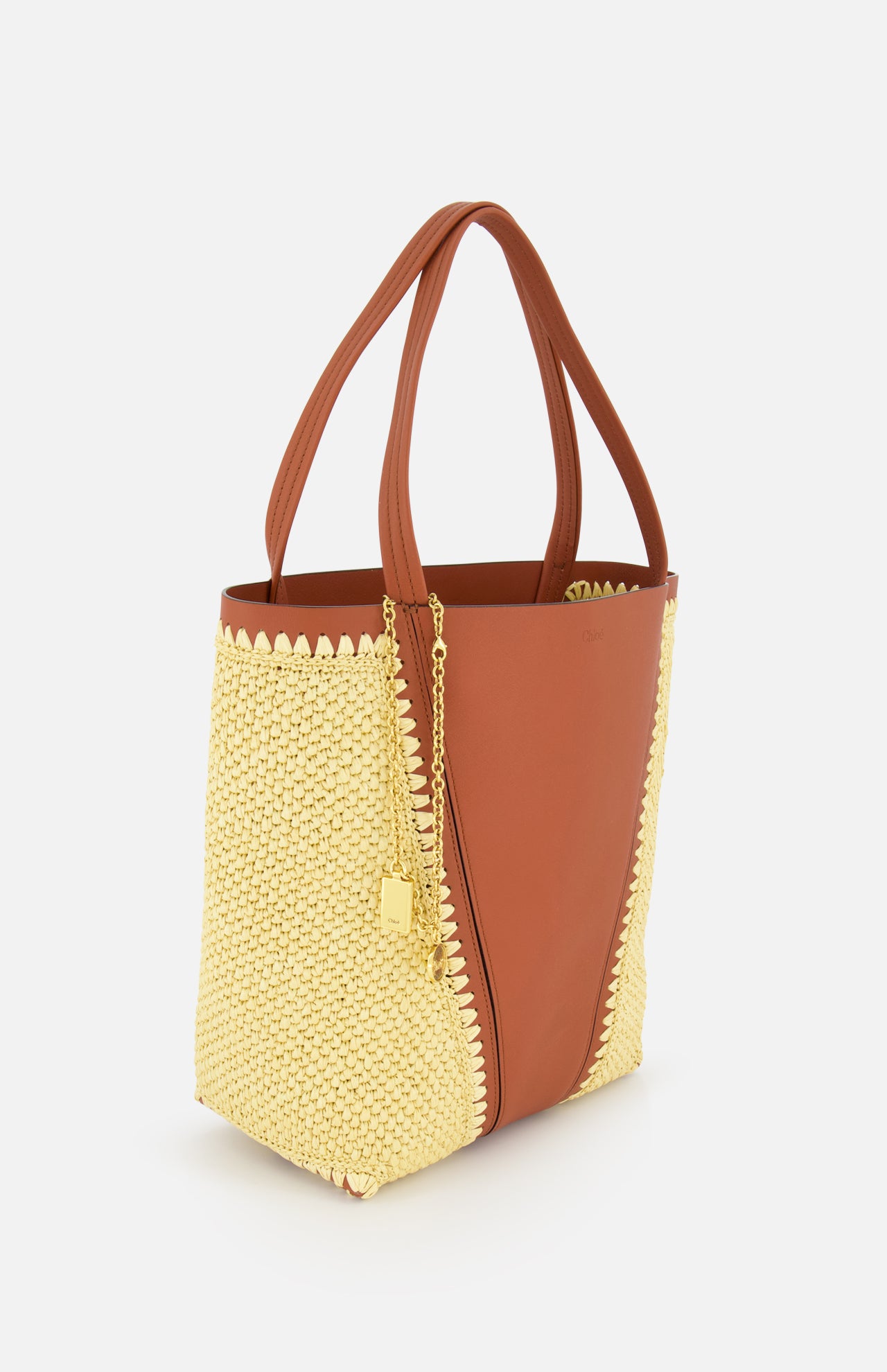 The CHLOÉ Woven Panels Spin Bag is a two-tone brown leather tote with yellow raffia-inspired woven side panels, double handles, and a gold chain padlock charm, shown against a white background.