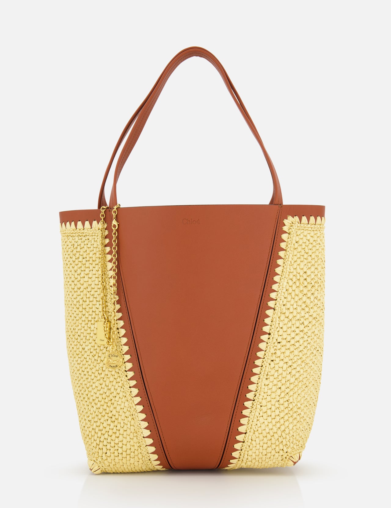 The CHLOÉ Woven Panels Spin Bag is a stylish brown leather tote with raffia-inspired woven sides, two brown handles, and a gold chain accessory, shown against a white background.