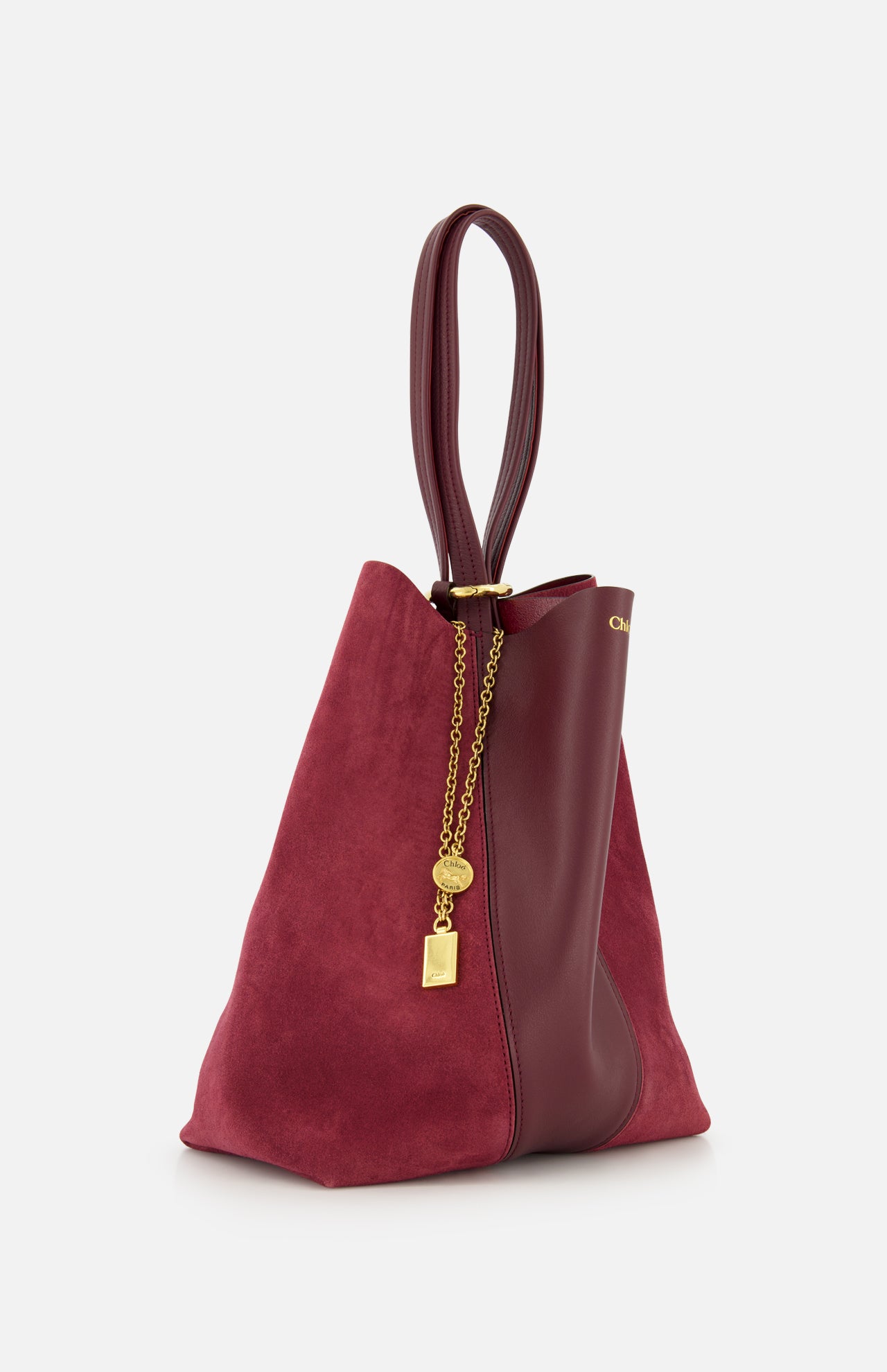 The CHLOÉ Leather and Suede Spin Bag combines burgundy suede and leather with elegant gold chain accents and a lock charm. Featuring a looped leather handle, this sophisticated tote also includes a removable bag chain for versatile styling options.