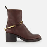 The CHLOÉ Dakota Riding Boot is a dark brown leather ankle boot with a chunky low heel, black sole, and gold metal harness detail—an equestrian-inspired style that adds a luxe touch to any outfit.