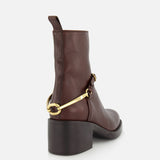 The Dakota Riding Boot by CHLOÉ is a dark brown leather ankle boot with a chunky heel, equestrian-inspired gold hardware at the back, and a pull tab, shown from the rear against a white background.