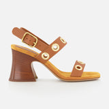 The Janis Slingback Grommet Heels by CHLOÉ feature brown leather with gold buckle and grommet accents, a yellow insole, and a flared wooden block heel, displayed in profile against a white background.