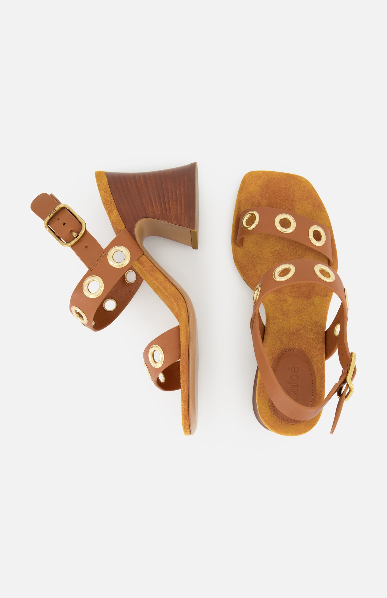 The Janis Slingback Grommet Heels by CHLOÉ are ginger brown sandals, crafted from supple leather with gold grommet accents, ankle straps, and chunky wooden block heels, displayed on a white background.